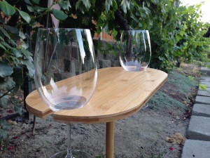 Bamboo Wine Table from Uncommon Goods holds two glasses of wine.